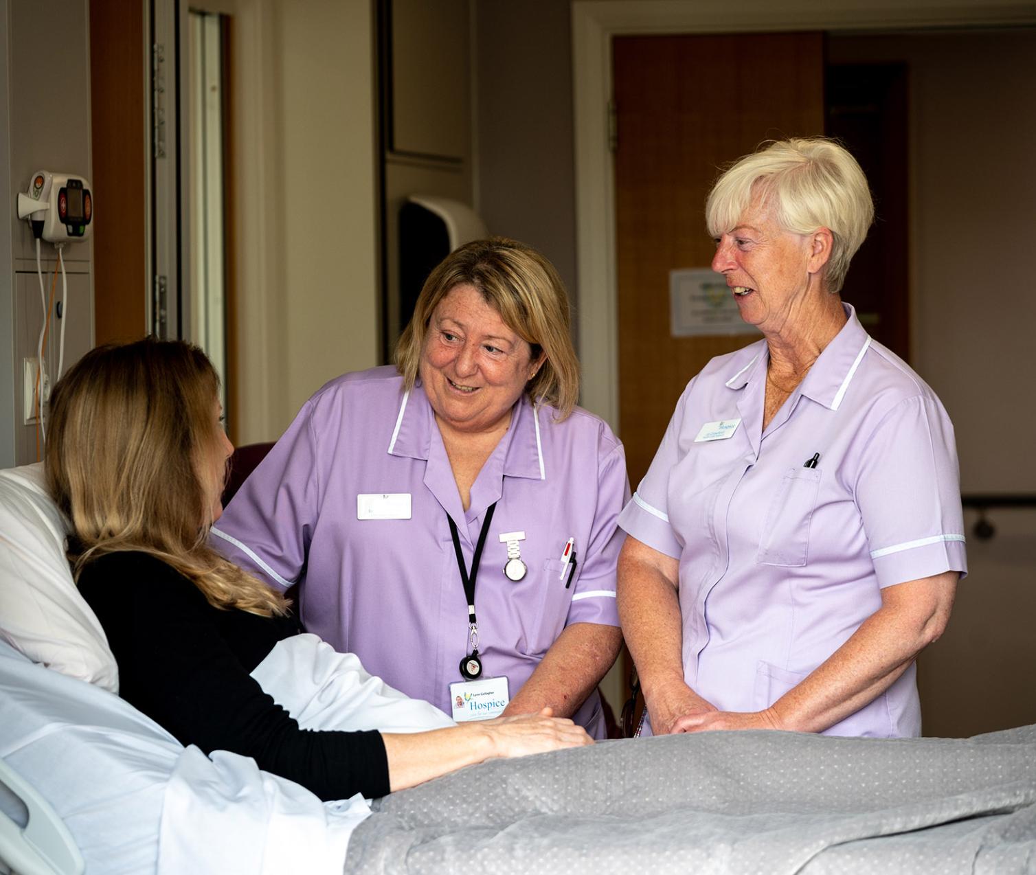 Two nurses talk to a patient lying in a bed